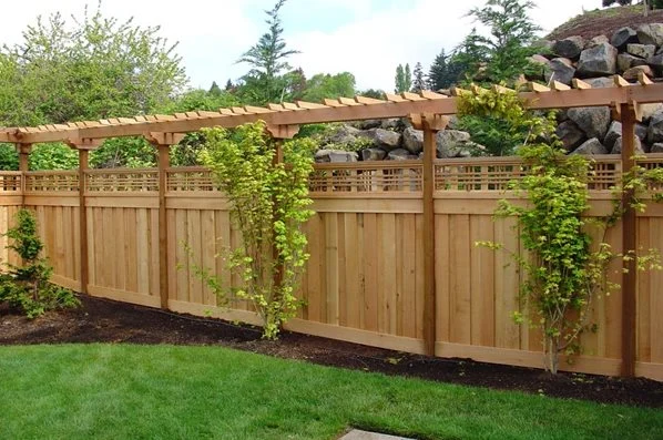 Custom cedar privacy fence with lattice top and pergola accent bordering a lawn and garden