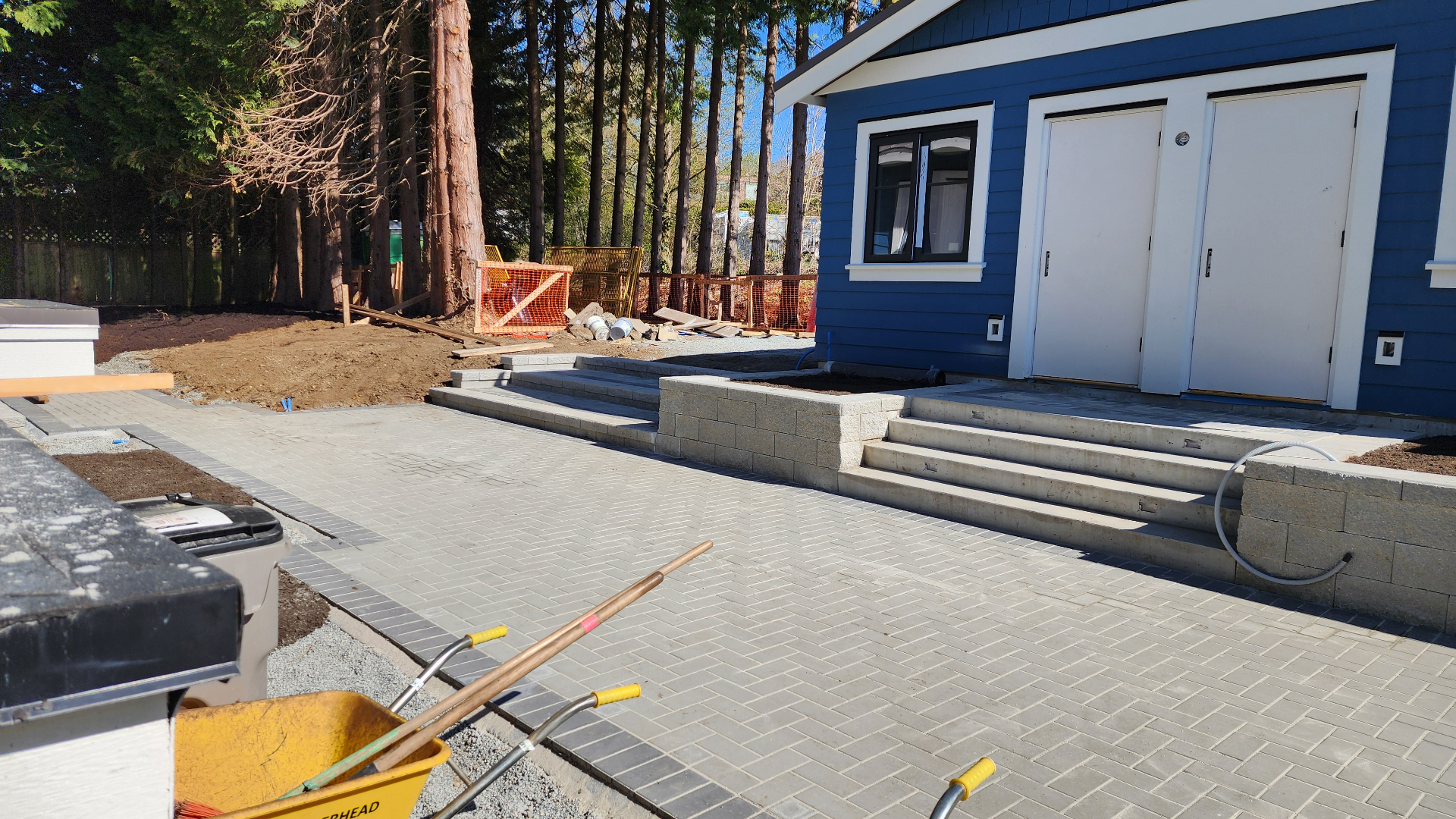 Paver walkway and steps with a block retaining wall and planter beside a new home
